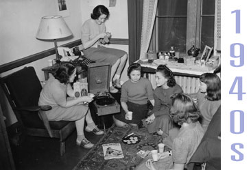 A Vassar dorm room from 1940s. Several girls sit on the fllor, sharing Ritz and other snacks