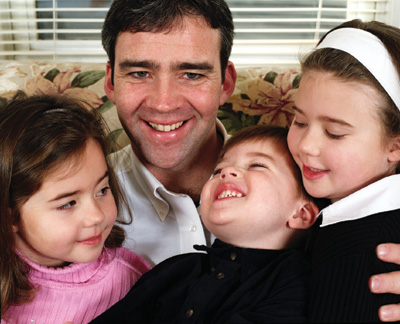 A man sits with his three children on his lap, smiling