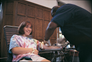 A student gets her blood drawn, sitting in a chair and smiling