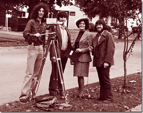 Three men and a woman stand around an old videocamera